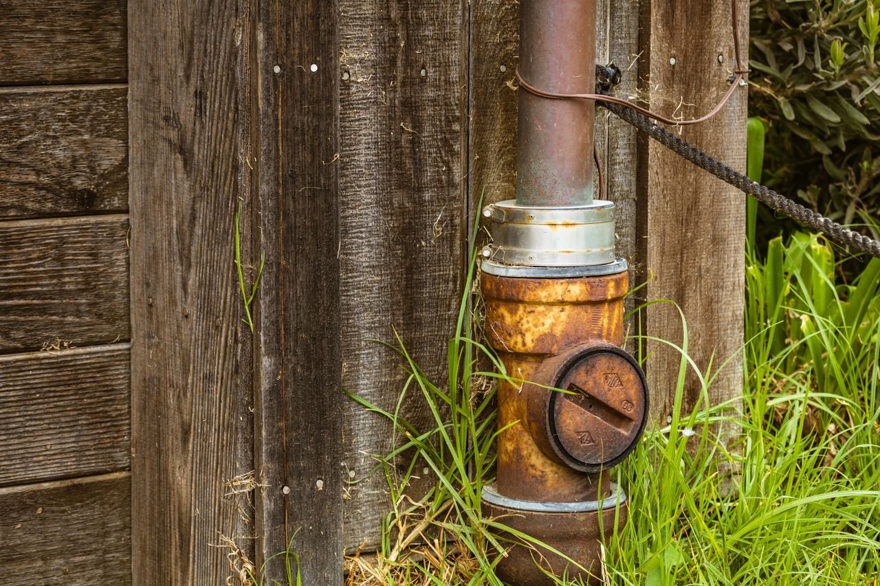 A close-up of a rusty pipe attached to an aged wooden barn in a rural setting.