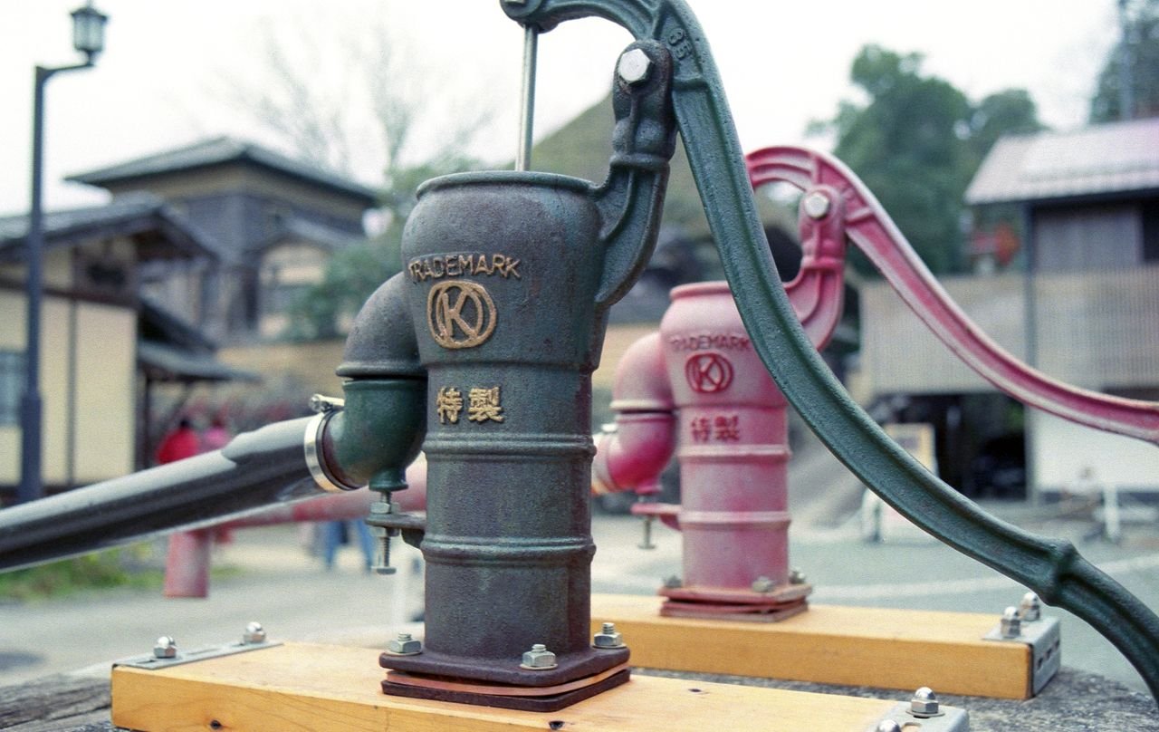 Close-up of a vintage water pump in a traditional Japanese setting, showcasing rustic charm.