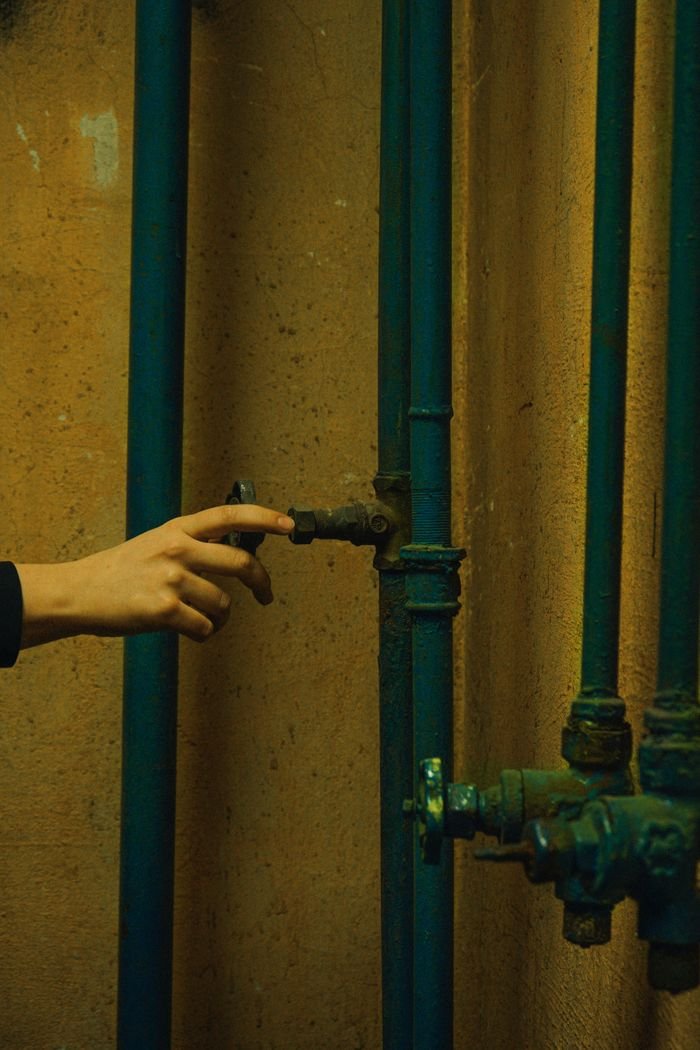 Close-up of a hand adjusting rusty metal pipes against a concrete wall indoors.