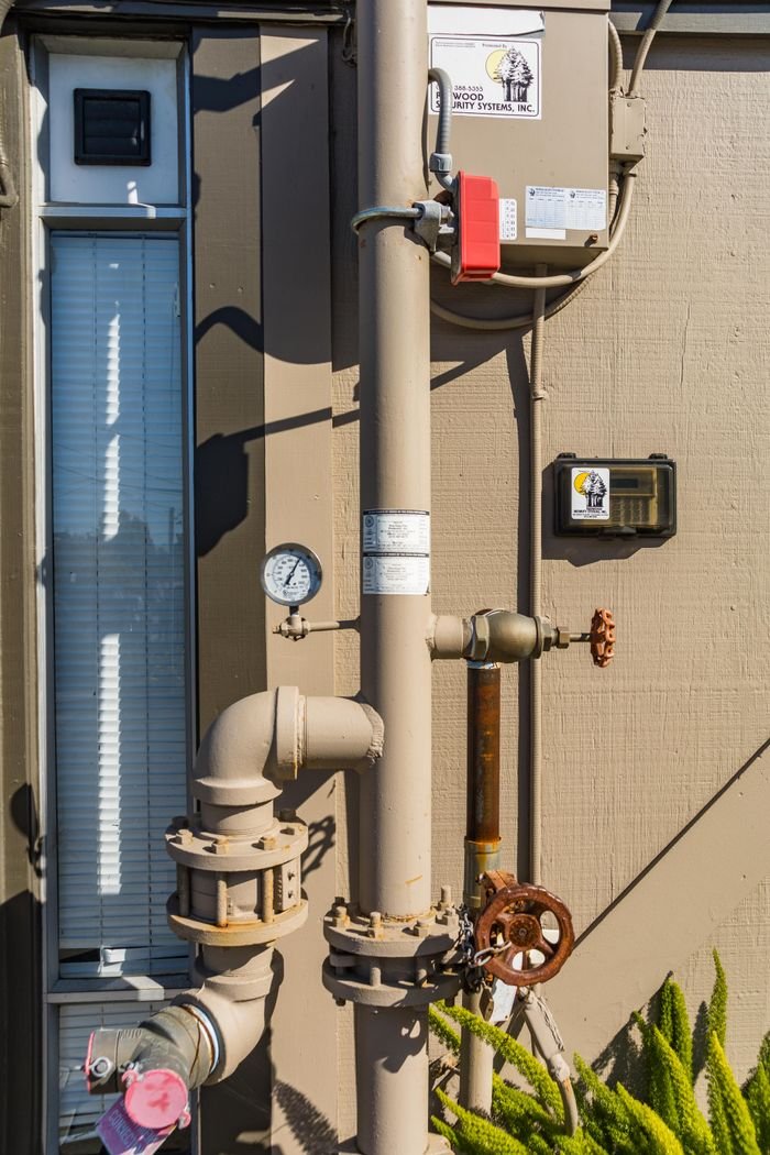 Close-up of industrial pipes and gauge system on an exterior building wall.