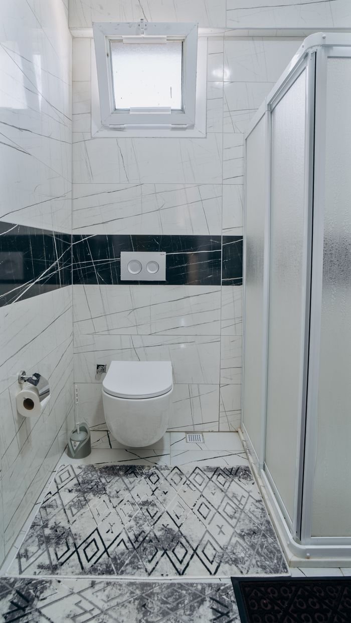 Contemporary bathroom featuring a white toilet, glass shower, and abstract tile design.