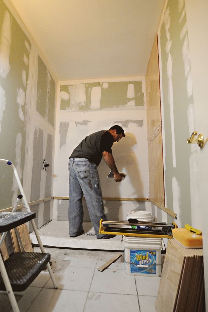 A man working on a bathroom renovation, applying drywall mud on interior walls.