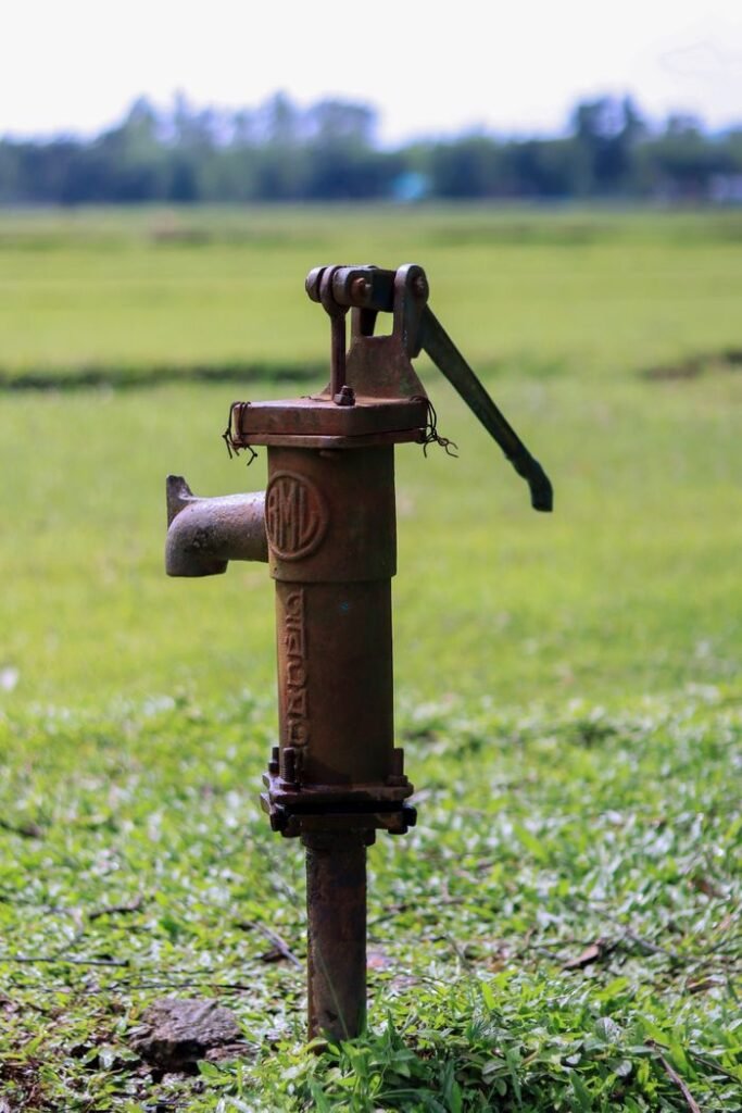 Rustic hand water pump surrounded by lush green field, representing traditional irrigation.