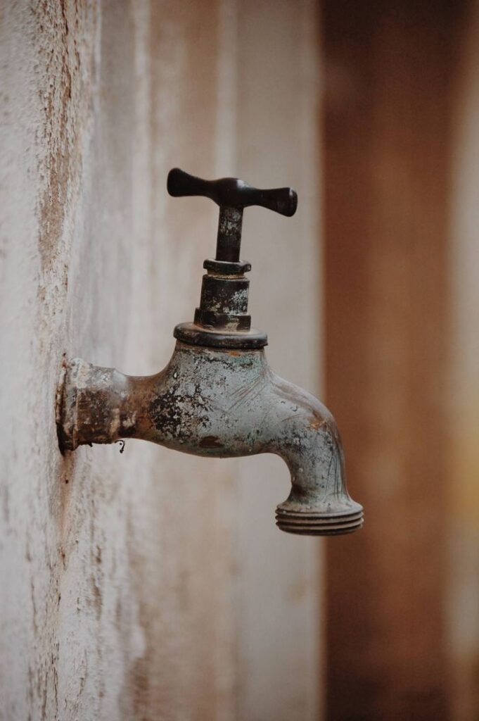 Old fashioned weathered metal tap installed on rough shabby wall in abandoned building