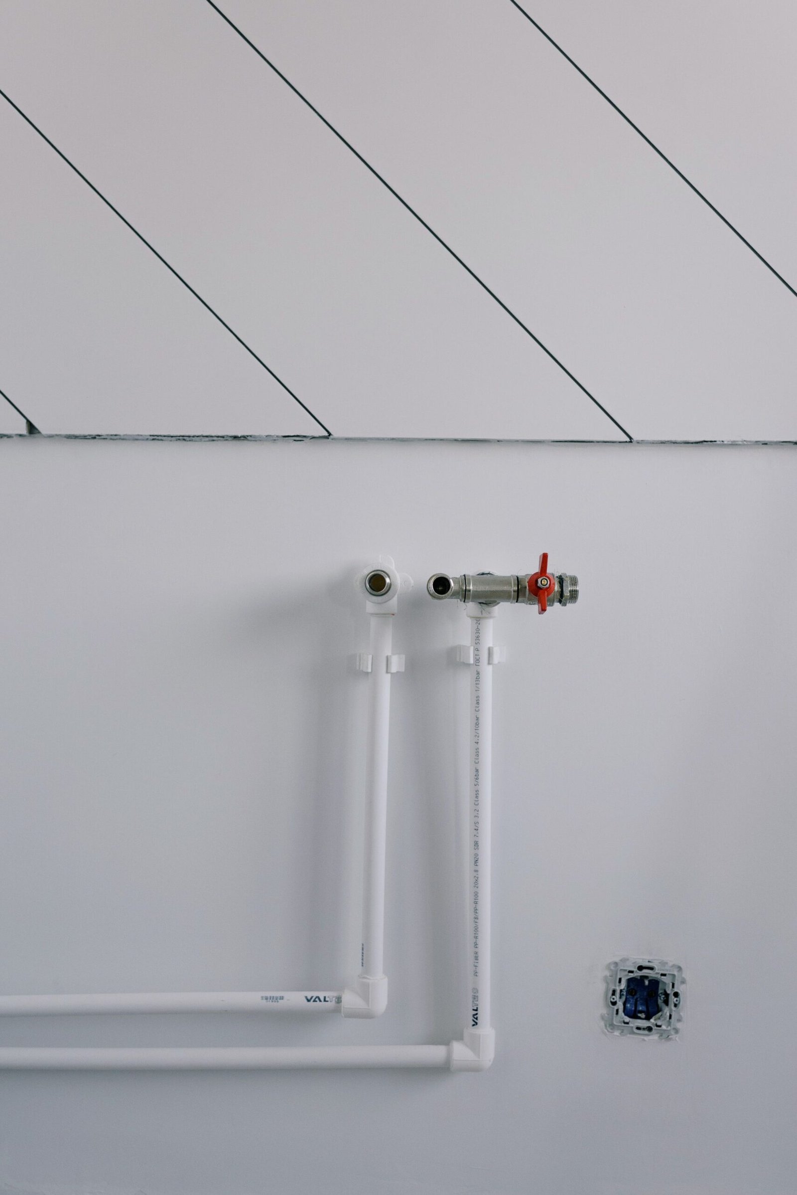 Long thin black slanted lines over pipes of radiator casting shadow on white wall in daytime