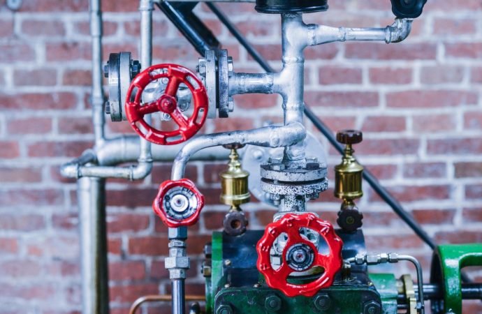 Close-up of industrial machinery with red valve handles and metal pipes against a brick wall.