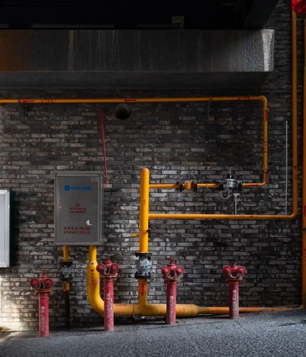 Brick wall with red hydrants and yellow piping in an urban alleyway setting.