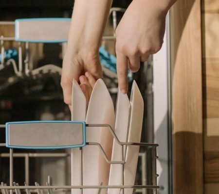 Hands loading clean dishes into an open dishwasher, demonstrating home appliance use.