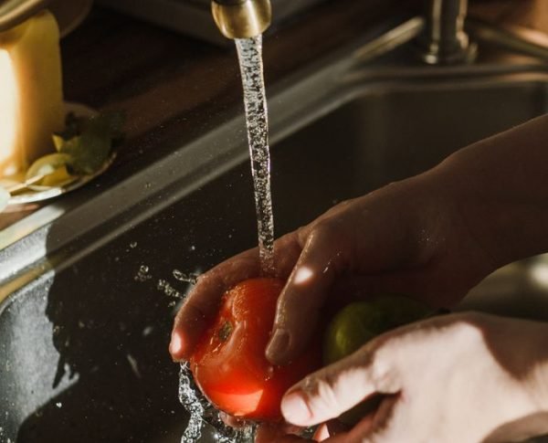 Close-up of hands washing a ripe tomato under a kitchen faucet. Perfect for themes of cleanliness and healthy living.
