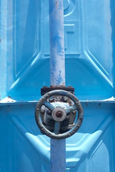 Close-up of a rusty valve on a blue industrial pipe outdoors in daylight.
