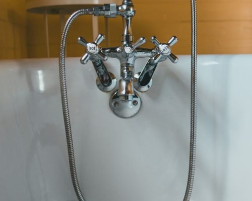 Elegant chrome vintage faucet and shower head in a white bathtub.