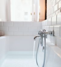 A modern white bathtub with chrome faucet and running water in a stylish tiled bathroom.